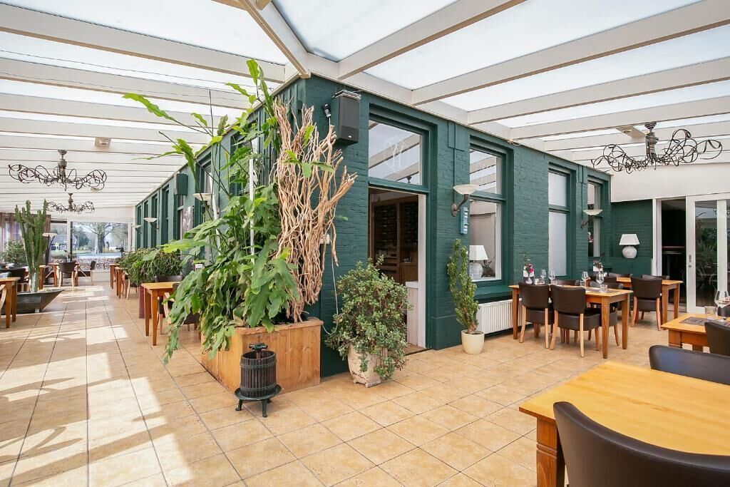 A spacious indoor area with a high ceiling, wooden tables and chairs, and potted plants.