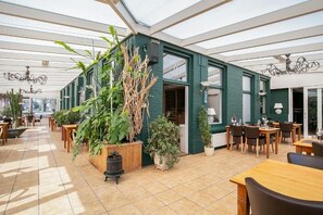 A spacious indoor area with a high ceiling, wooden tables and chairs, and potted plants. - De Wapser Herberg (Wapse)
