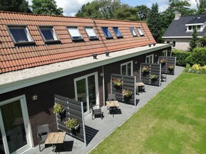 A modern building with a sloped roof, multiple windows, and a patio area with outdoor seating and planters. - De Wapser Herberg (Wapse)