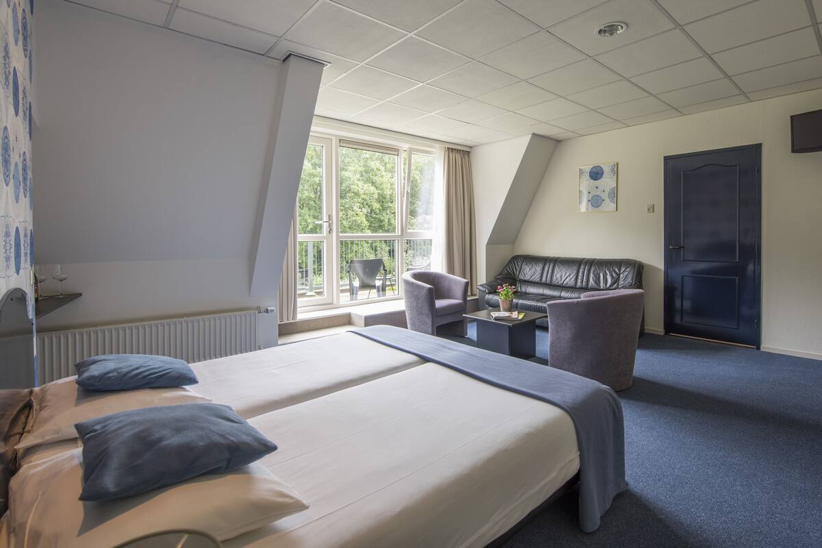 A hotel room with a large bed, a desk with a chair, a sofa, and a TV mounted on the wall.