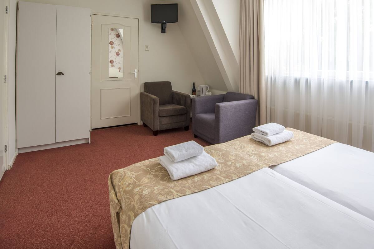 A hotel room with a bed, two armchairs, a desk, and a TV.