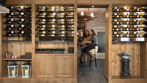 A wine cellar with wooden shelves holding numerous wine bottles. There are two people seated at a table in the center, surrounded by wine racks. - De Wapser Herberg (Wapse)
