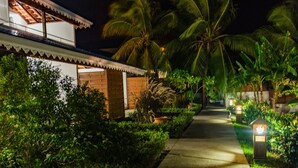 A pathway leading to a building with a traditional architectural style, surrounded by lush greenery and palm trees. - Makare Lagoon Club (Le Vauclin)