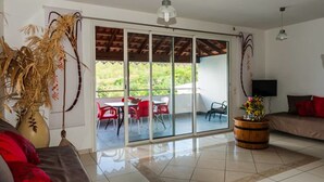 A spacious living area with a sliding glass door leading to an outdoor patio, a sofa, a coffee table, and a potted plant. - Makare Lagoon Club (Le Vauclin)
