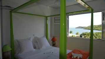 A bedroom with a bed, a nightstand, a lamp, and a view of the sea.