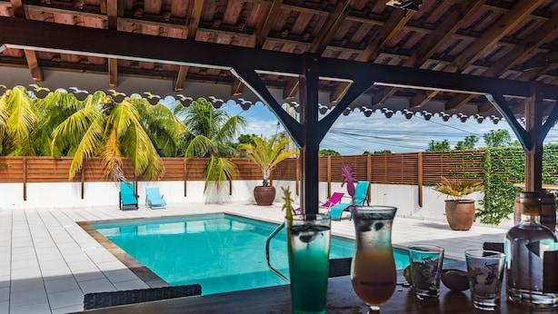 A poolside area with a wooden pergola, lounge chairs, and a bar with drinks. - Makare Lagoon Club (Le Vauclin)