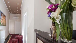 A hallway with a red carpet, a wooden reception desk, a glass vase with flowers, and two red suitcases. - DVE Suite Rome (Rome)