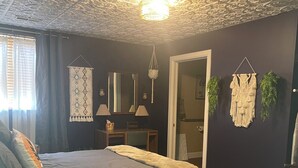 Ein Schlafzimmer mit einem großen Bett, Holzboden, Decke mit aufwendigen Mustern und einer Wanddekoration aus Makramee.