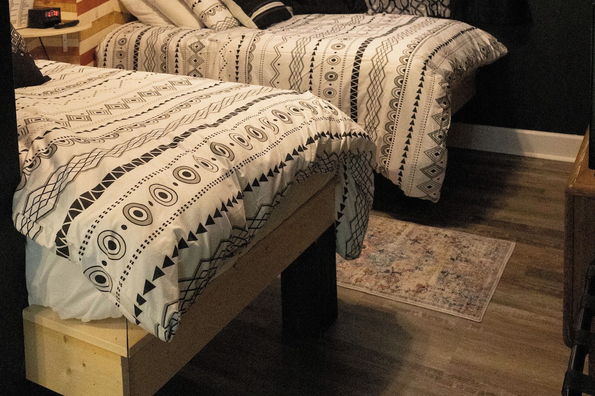 A bedroom with two beds, patterned bedding, a decorative ceiling, and a small table.