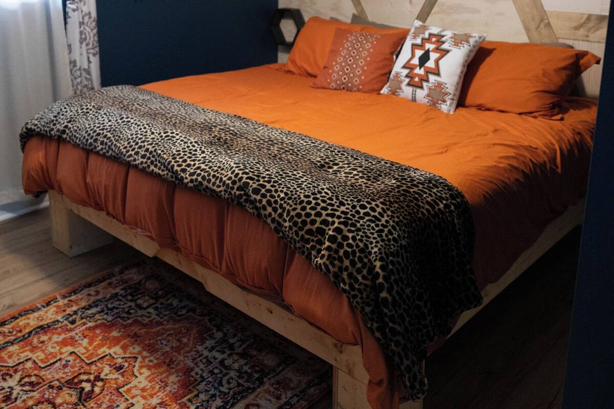 A bedroom with a wooden bed, orange bedding, a patterned rug, and decorative wall art.