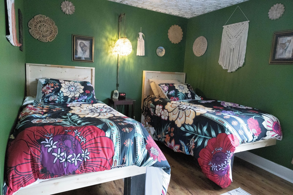 A room with two beds, green walls, and decorative wall hangings.