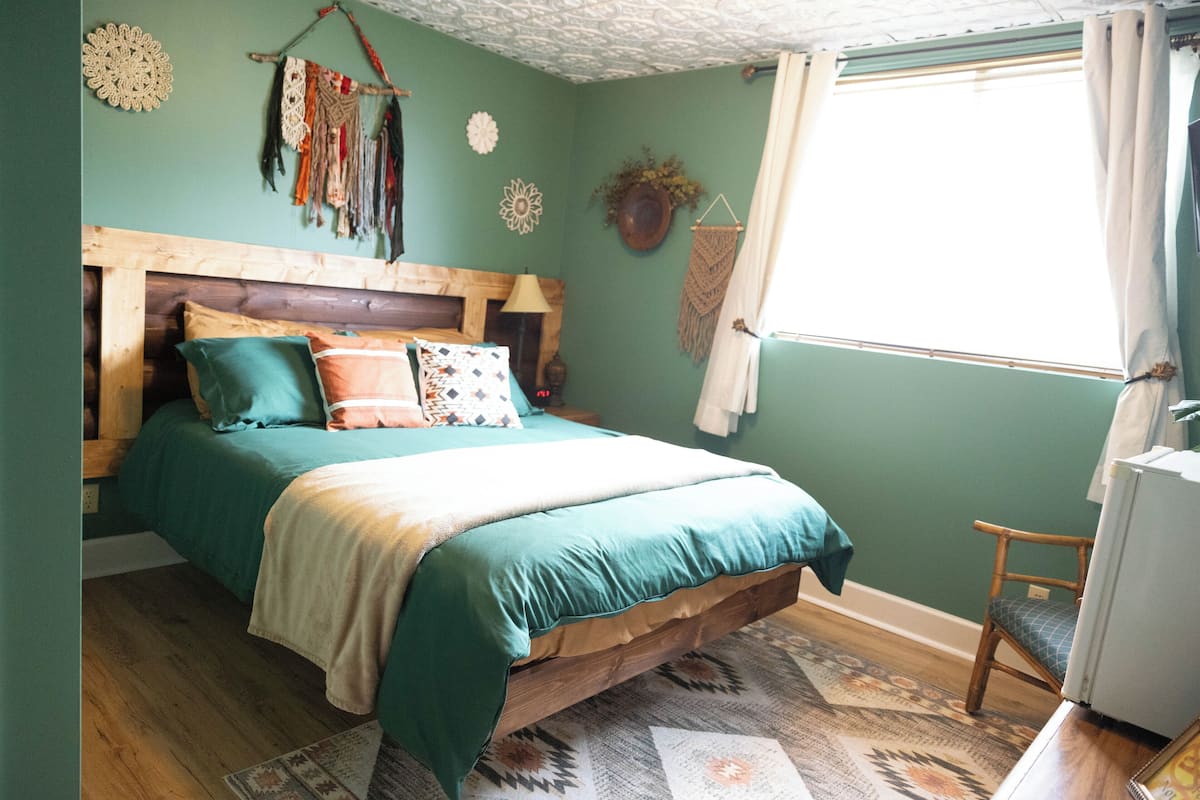 A bedroom with a wooden headboard, a bed with teal bedding, a patterned rug, and a window with curtains.