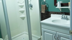 A bathroom with a glass-enclosed shower, a sink, and a mirror. - Monroe Street Suites (Pittsfield)