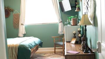 A cozy bedroom with a bed, a desk, a chair, and a round ottoman.