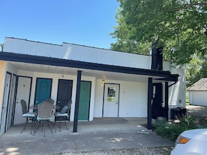 A white building with a covered porch, numbered doors, and outdoor seating.