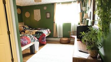 A room with a bed, a desk, a chair, a plant, and a window with curtains.
