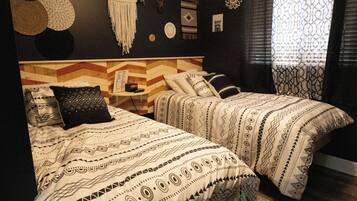 Una habitación con dos camas, cada una con ropa de cama estampada, un cabecero de madera y una mesita de noche pequeña con una lámpara.