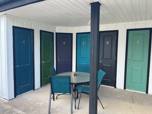 Uma área de estar coberta ao ar livre, com mesa e cadeiras, cercada por portas numeradas de 1 a 5.