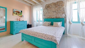 A bedroom with a bed, a dresser, a painting, and a stone wall. - Heritage hotel Chersin (Fazana)