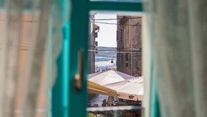 A view through a window with a green frame, revealing a street with buildings and a white umbrella. - Heritage hotel Chersin (Fazana)