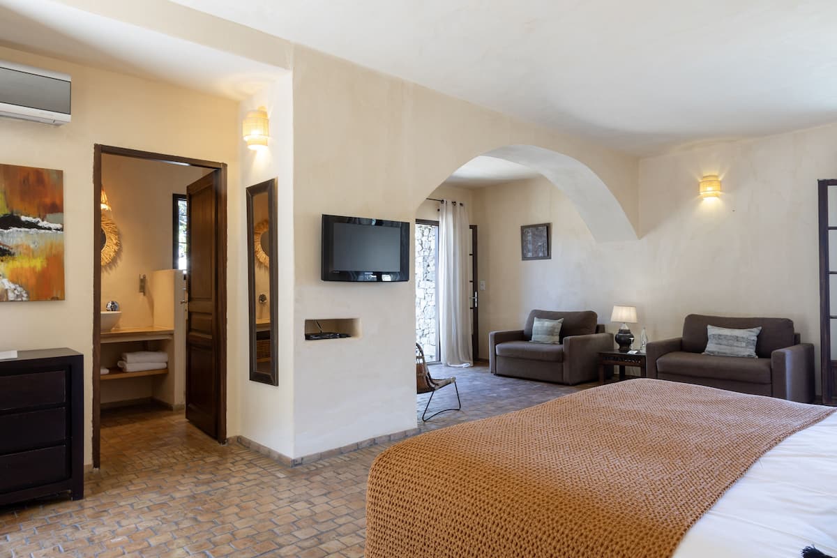 A hotel room with a large bed, two sofas, a TV, and a bathroom visible through an open door.
