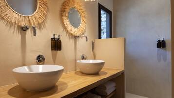 Ein Badezimmer mit zwei großen weißen Waschbecken, einem Holz-Waschtisch und zwei Wandspiegeln mit Fransenverzierungen.