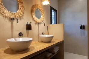 A bathroom with two large white sinks, wooden vanity, and two wall-mounted mirrors with fringe designs. - Hôtel Case Latine (Lama)