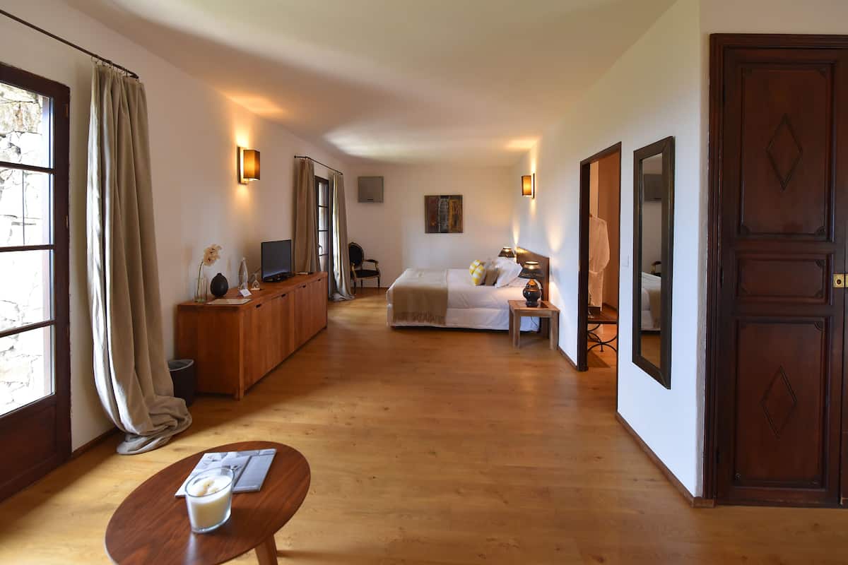 A hotel room with a bed, bedside table, lamp, and a view of the hallway.