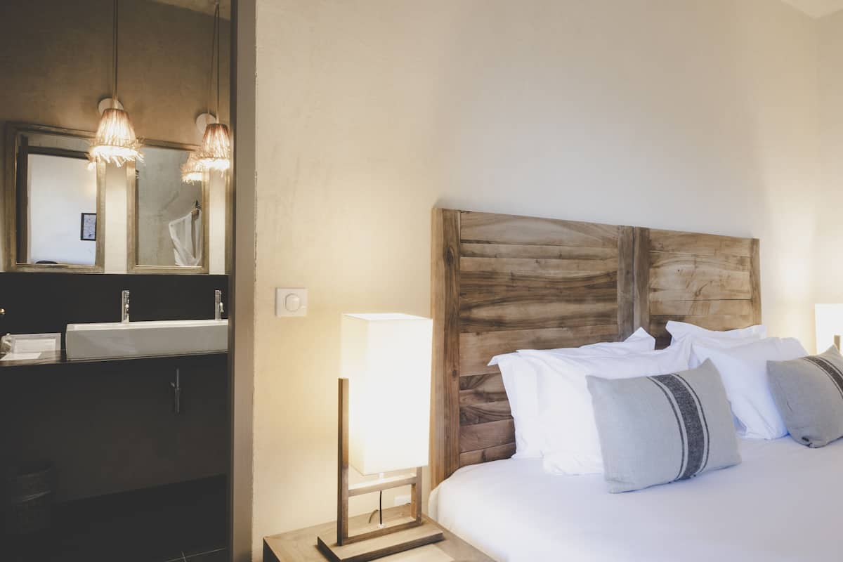 A hotel room with a wooden headboard, a large mirror, a bedside table with a lamp, and a bed with pillows.