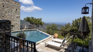 Un edificio de piedra con piscina y sillones de descanso con vistas a un paisaje pintoresco.