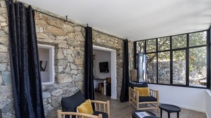 Una habitación acogedora con paredes de piedra, un sofá de madera con un cojín amarillo, un televisor y un ventanal con vistas al exterior.