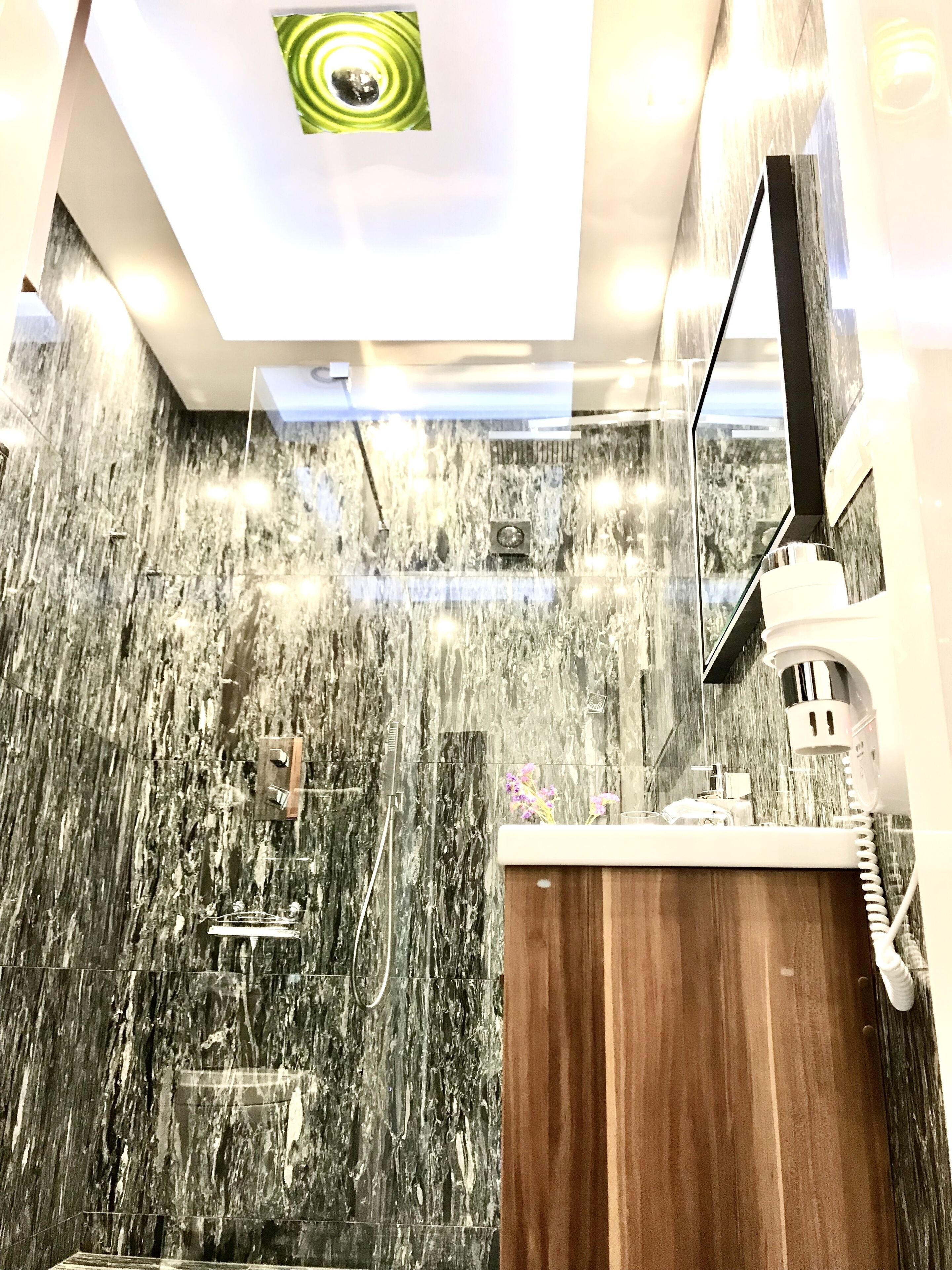 A modern bathroom with a marble wall, a wooden vanity, and a shower area.