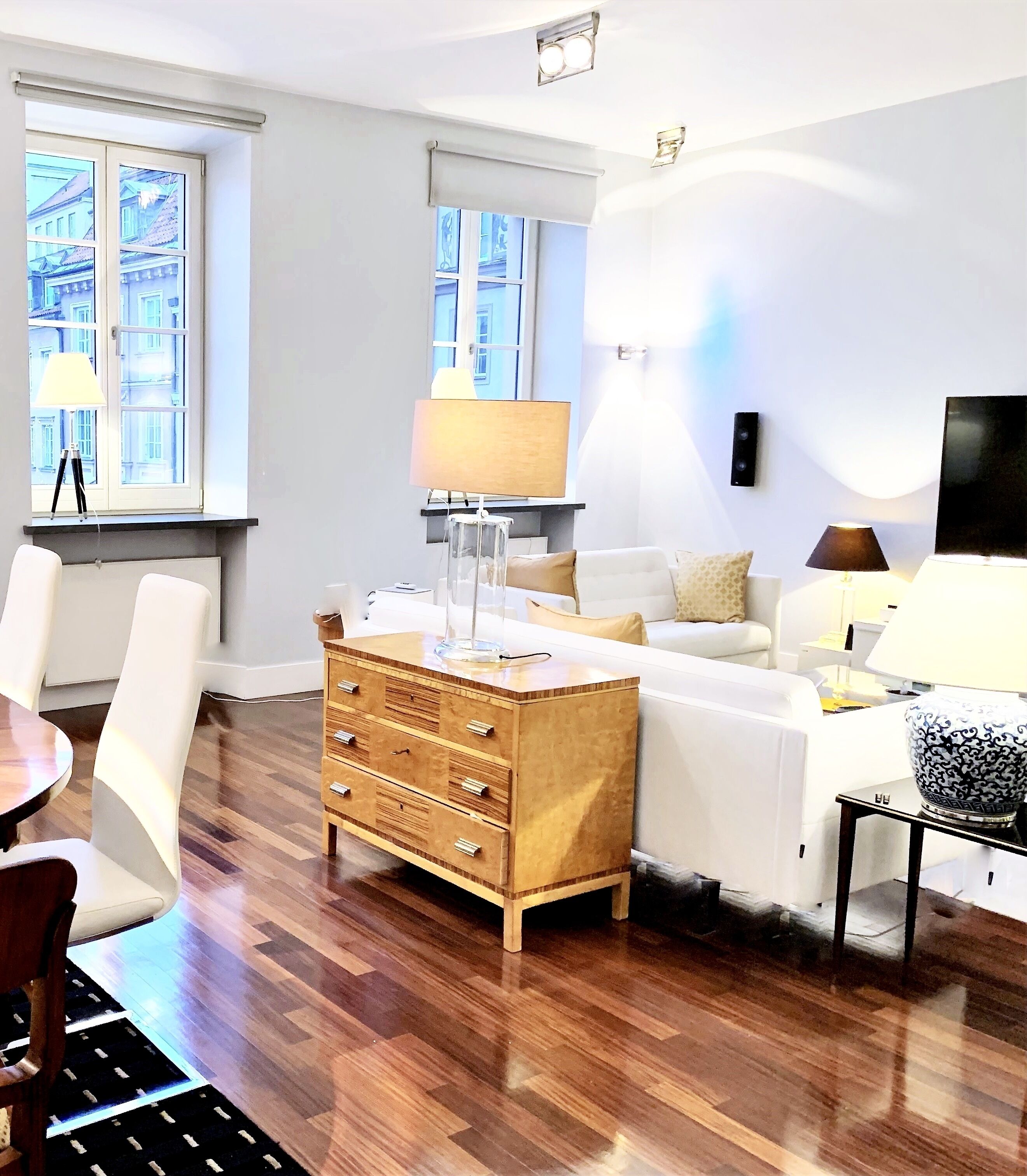 A modern living room with a wooden chest of drawers, a white sofa, and a dining area with a table and chairs.