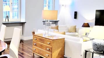 A modern living room with a wooden chest of drawers, a white sofa, and a dining area with a table and chairs.
