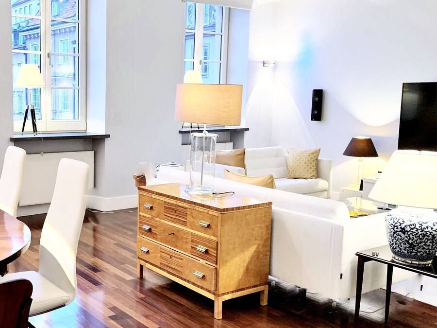 A modern living room with a wooden chest of drawers, a white sofa, and a dining area with a table and chairs.