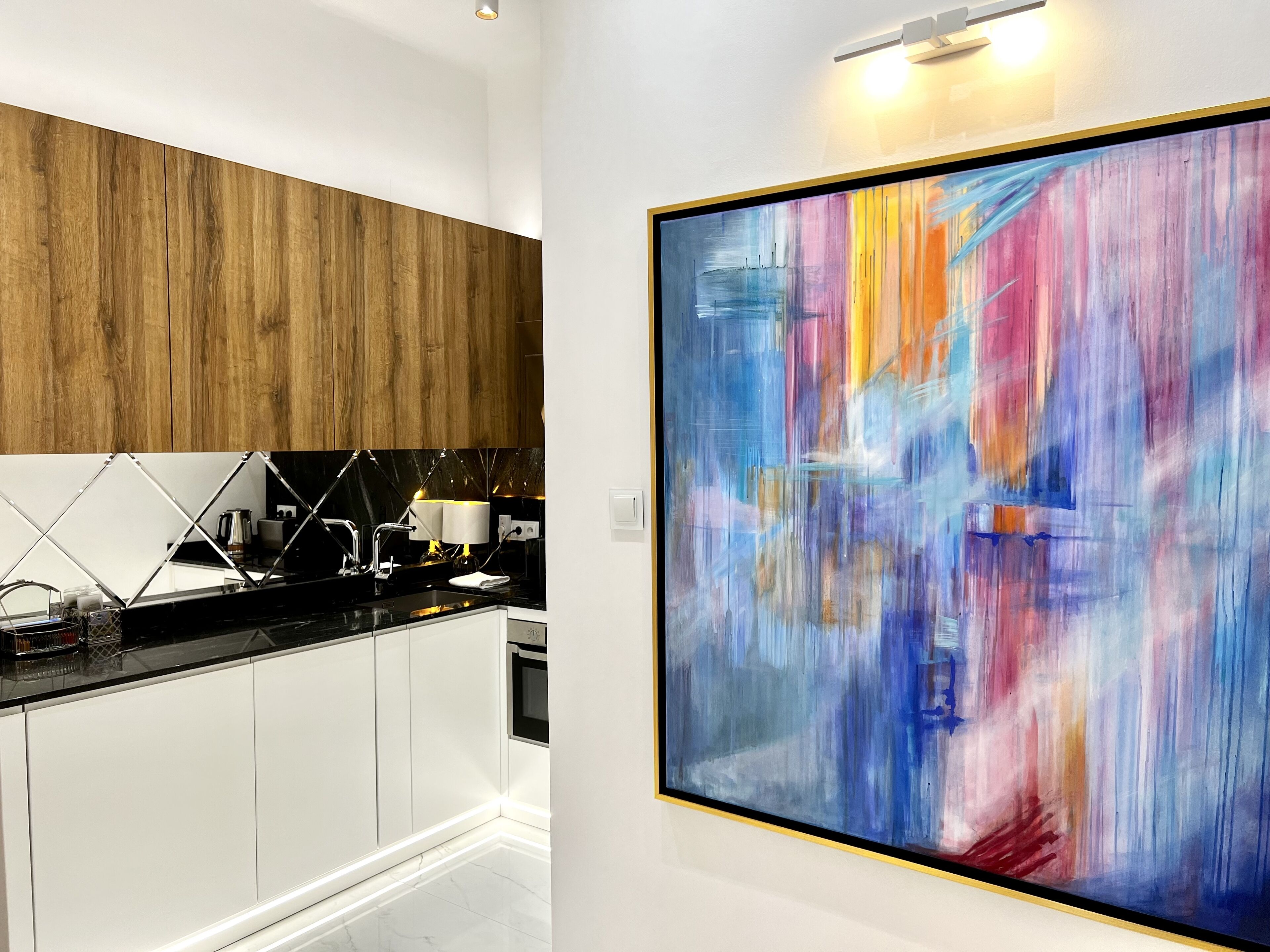 A modern kitchen with white cabinets, a black countertop, and a large abstract painting on the wall.