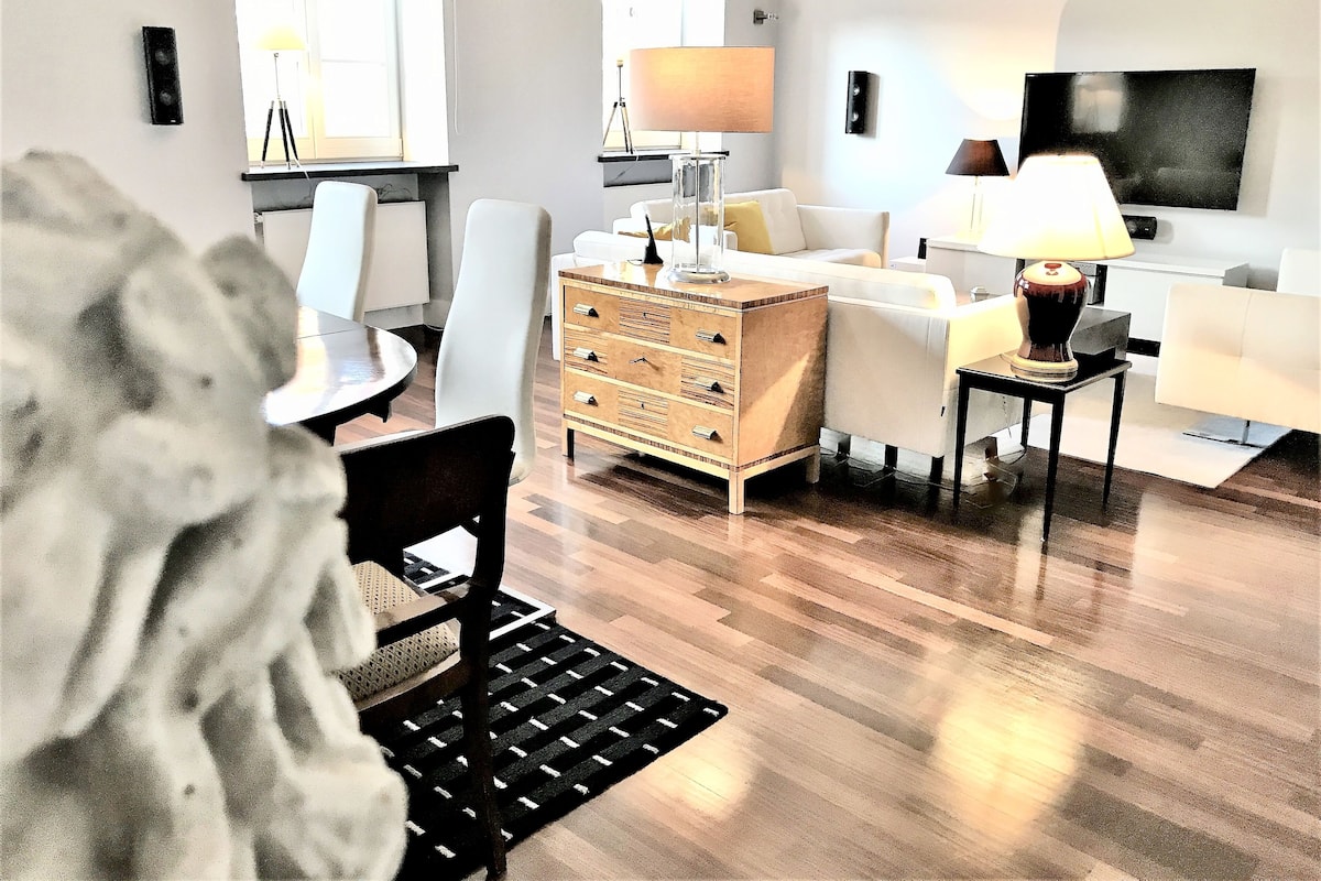 Una sala de estar moderna con piso de madera, muebles blancos, una mesa de centro, un sofá, un televisor y una lámpara.