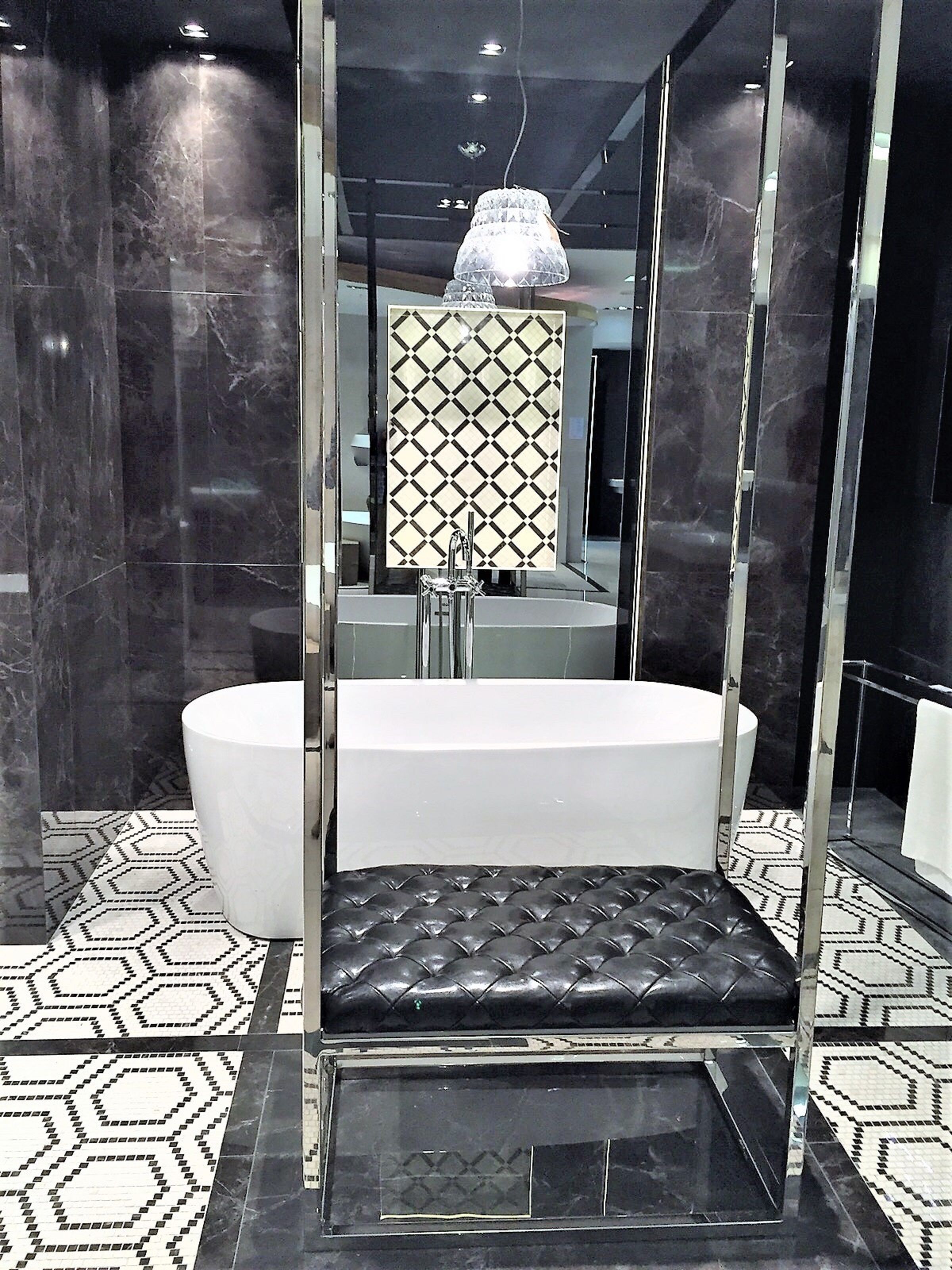 A modern bathroom with a large mirror, a black leather bench, and a white bathtub.