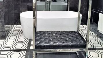 A modern bathroom with a large mirror, a black leather bench, and a white bathtub.