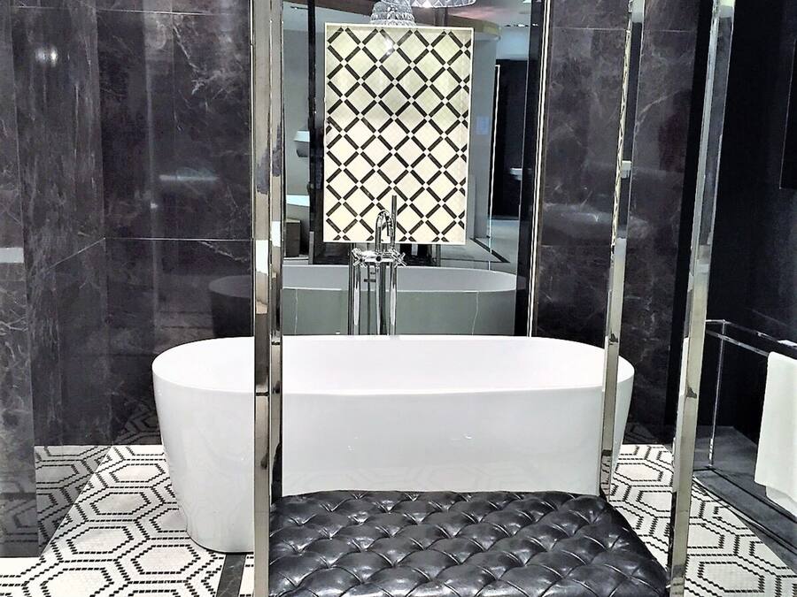 A modern bathroom with a large mirror, a black leather bench, and a white bathtub.