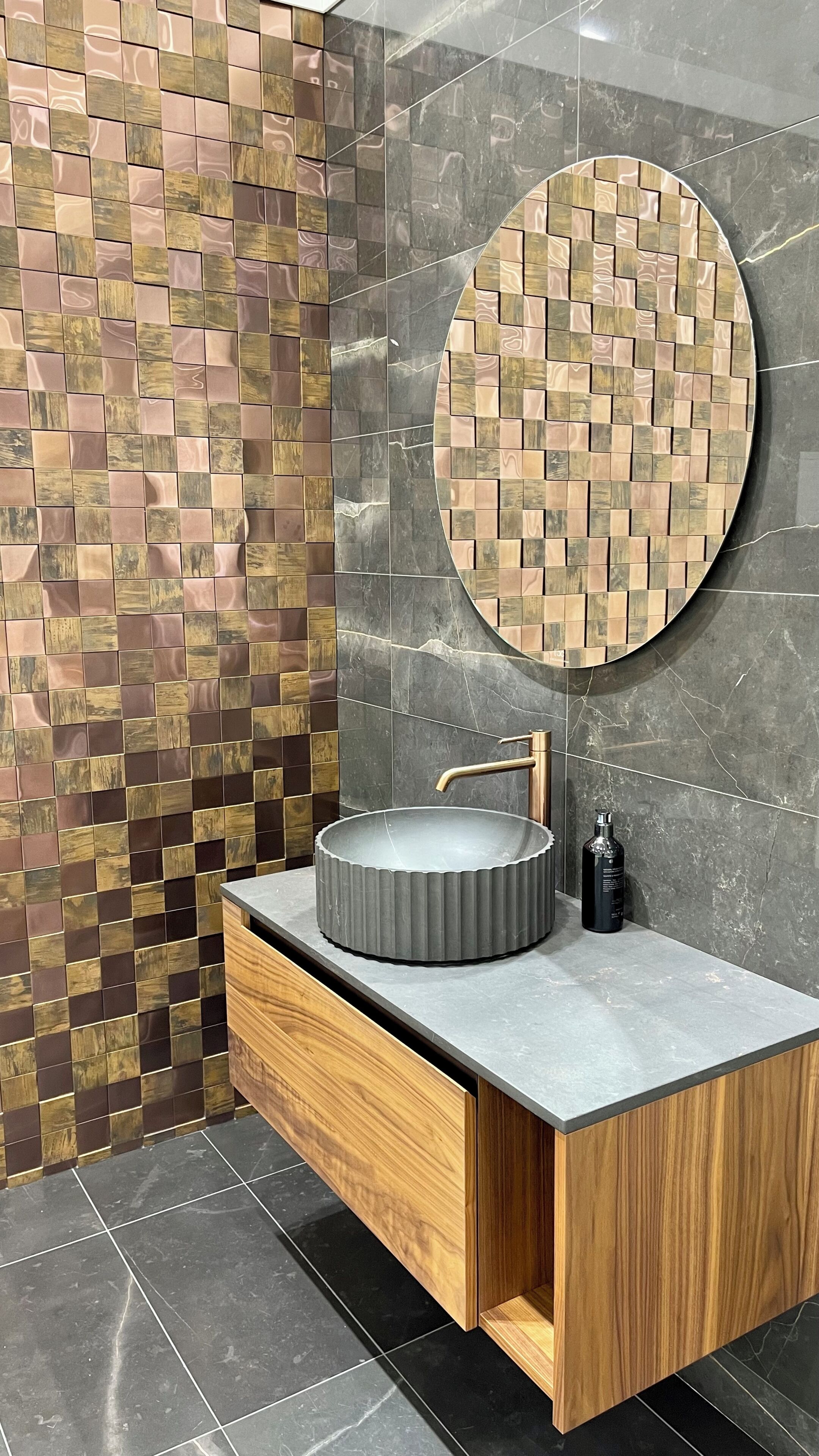 A bathroom with a round mirror, a round sink, a wooden cabinet, and a tiled wall.