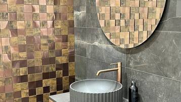 A bathroom with a round mirror, a round sink, a wooden cabinet, and a tiled wall.