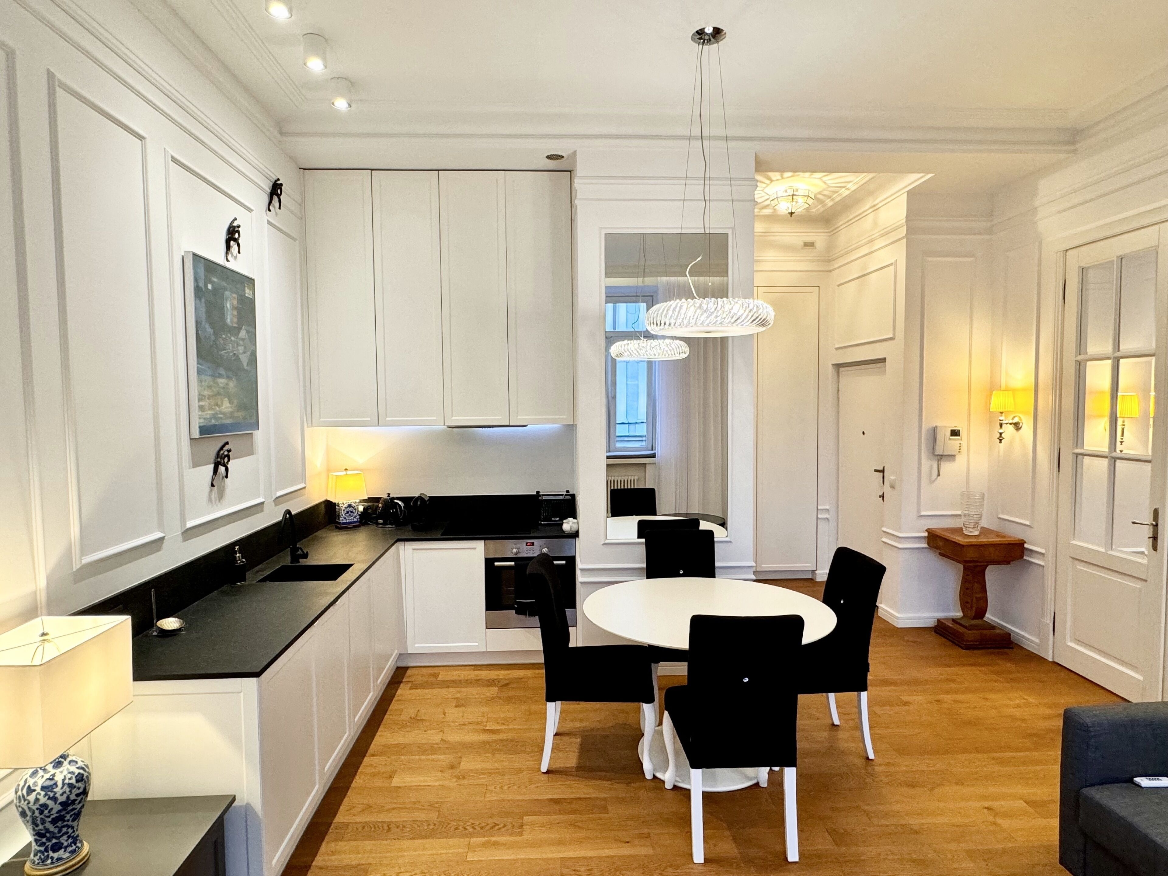 A modern kitchen with white cabinetry, a black countertop, and a dining area with a round table and black chairs.