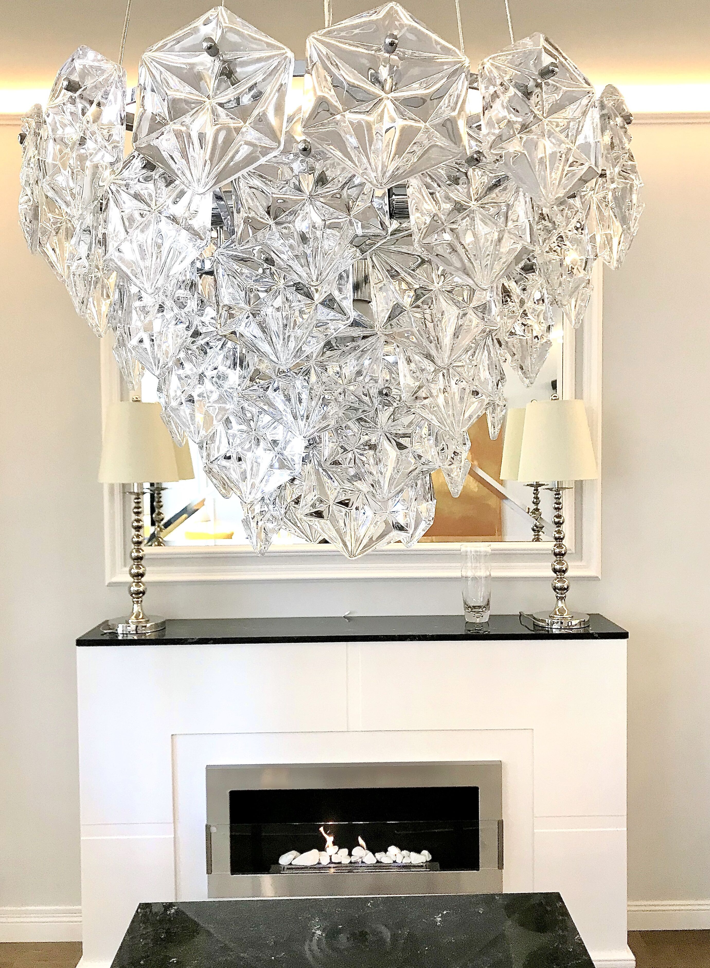 A chandelier made of clear crystal pieces hanging over a fireplace.