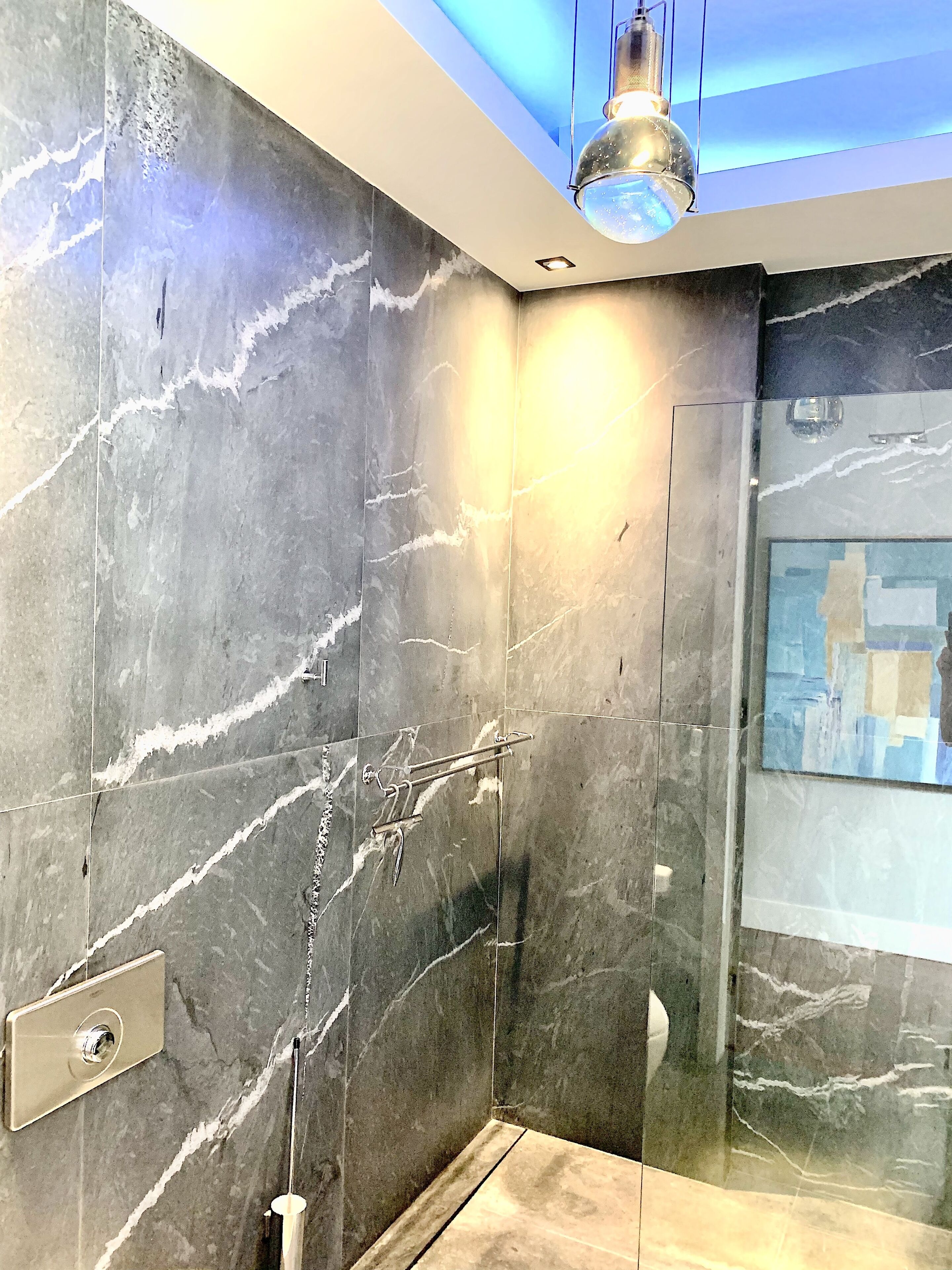 A modern bathroom with a glass shower enclosure, marble walls, and a ceiling light fixture.