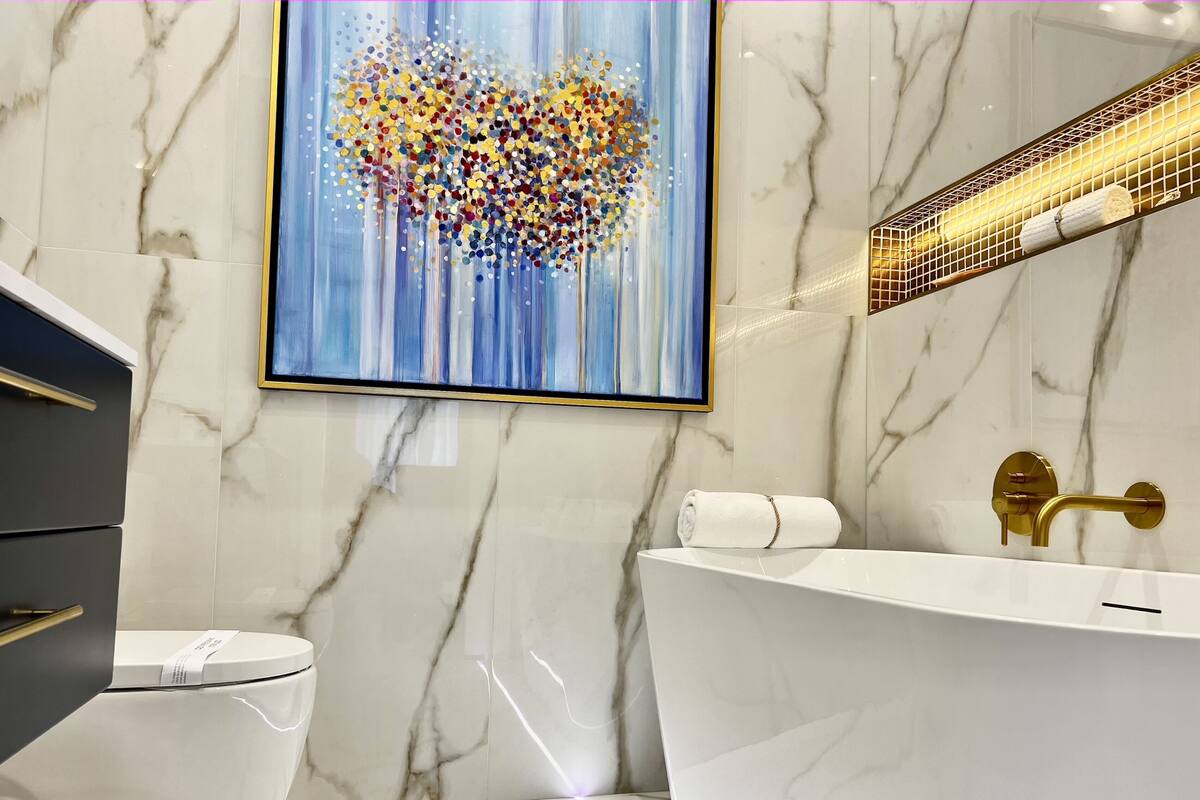 Un baño moderno con un lavamanos de mármol blanco, un grifo dorado y un cuadro abstracto enmarcado en la pared.