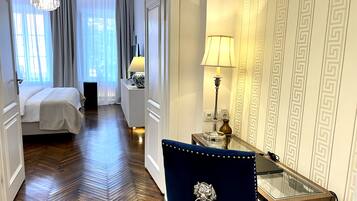 Une chambre d’hôtel avec un lit, un bureau doté d’une lampe, une chaise et un couloir menant à une autre pièce.