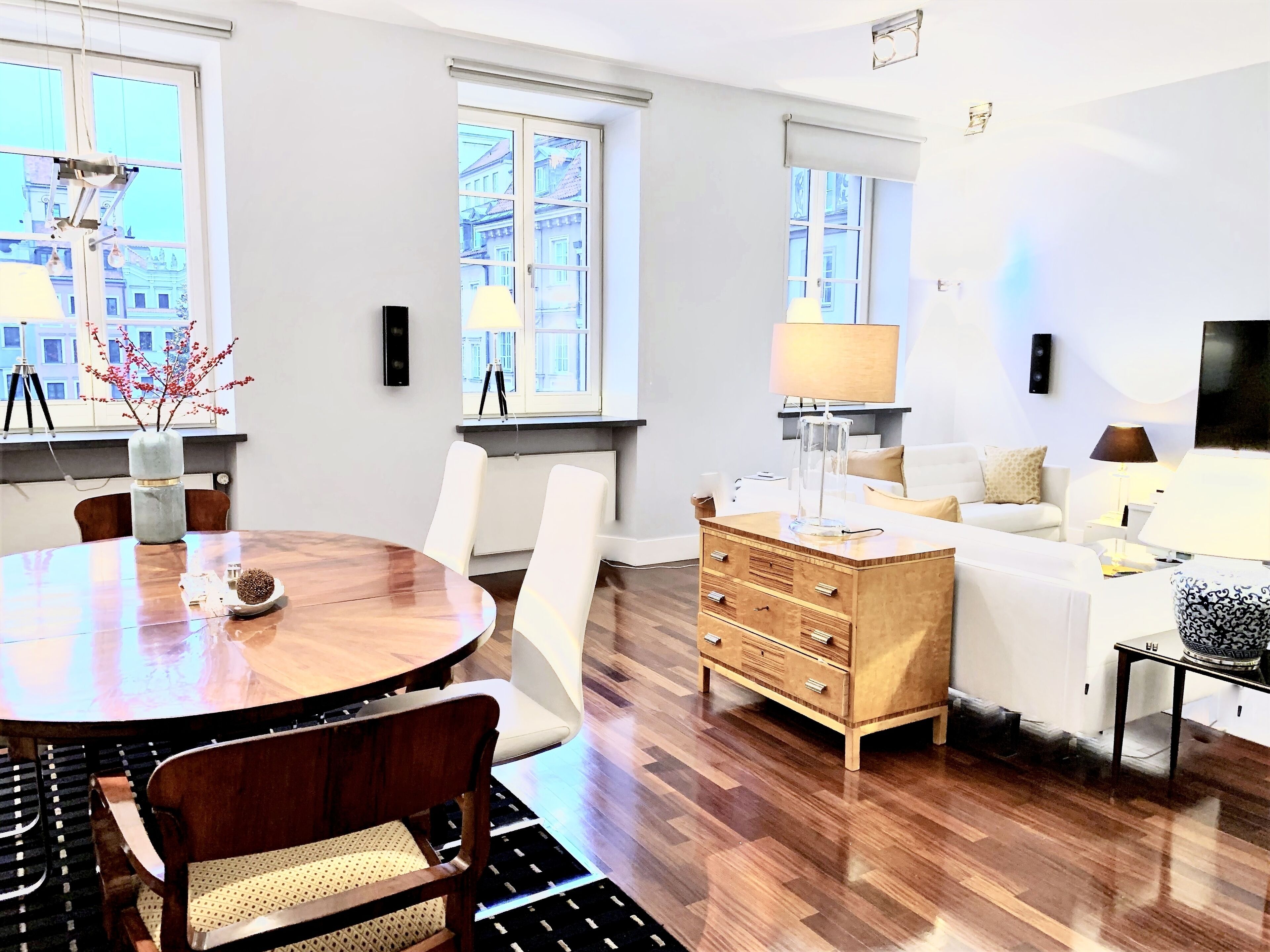 Una sala de estar moderna con una mesa de comedor de madera, sillas blancas, un aparador de madera y un sofá blanco.