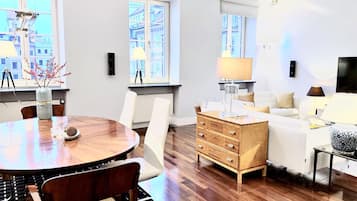 Una sala de estar moderna con una mesa de comedor de madera, sillas blancas, un aparador de madera y un sofá blanco.