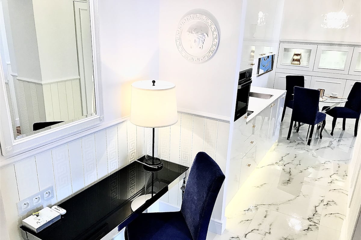 Una habitación de hotel moderna con un escritorio negro, una silla azul, una lámpara blanca y un suelo de mármol.